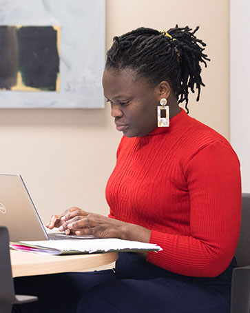 A student sits and looks at a laptop. This is a side profile photo of the student and surrounding space